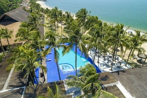 A resort with a pool surrounded by palm trees, a beach, and a view of the ocean. - Portobello Hotel Resort AND Safari (Mangaratiba)