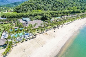 Vista aérea de um resort com praia, área de piscina e vegetação exuberante.