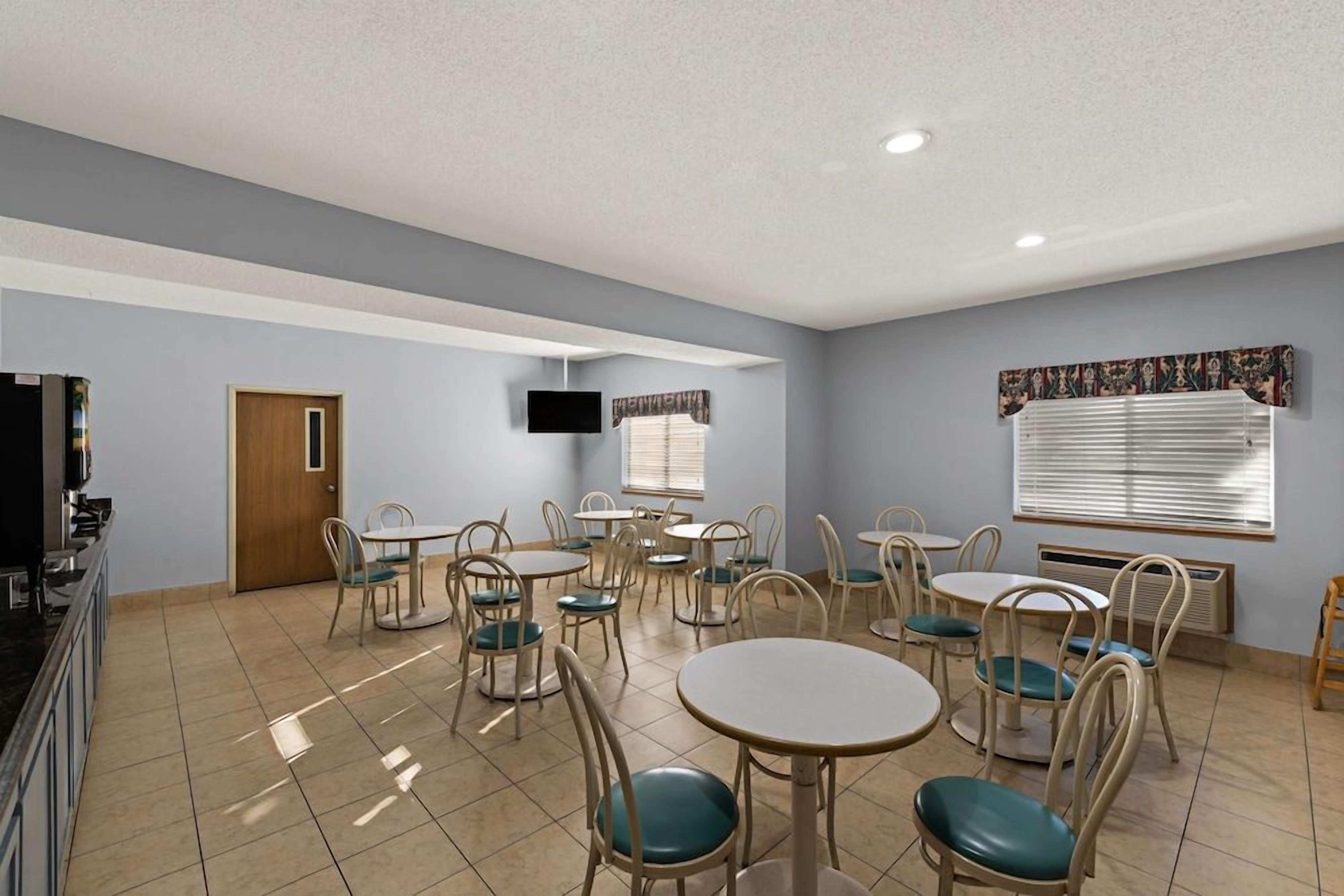 A dining area with multiple tables and chairs, a television mounted on the wall, and a door leading to another room.