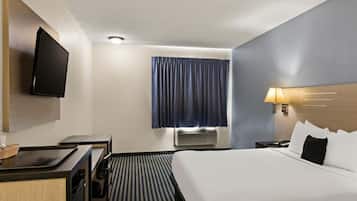 A hotel room with a bed, a desk, a television, a window with curtains, and an air conditioning unit.