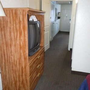 Un pasillo con un armario de madera, un televisor y una puerta que da a otra habitación.