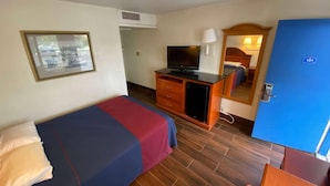 Ein Hotelzimmer mit einem Bett, einem Schreibtisch mit Fernseher, einem Spiegel und einer Tür mit der Nummer 101.