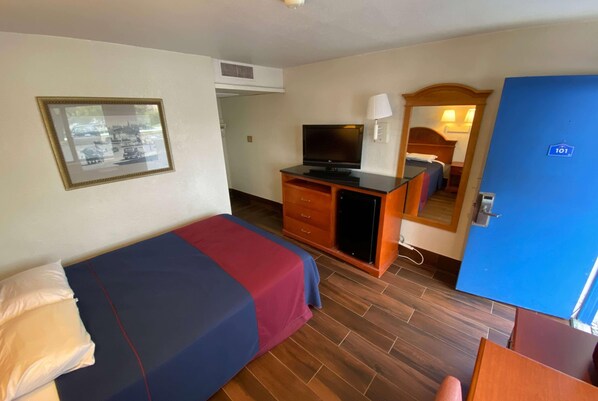 A hotel room with a bed, a desk with a television, a mirror, and a door marked with the number 101.