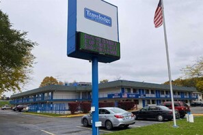 A Travelodge motel with a digital signboard, a parking lot, and an American flag.