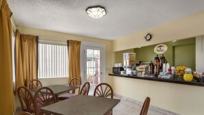 A dining area with a table and chairs, a coffee station with various beverages and food items, and a clock on the wall. - Super 8 By Wyndham Ridgecrest (Ridgecrest)