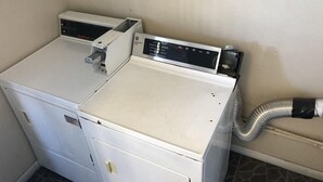 A laundry room with two stacked washers and dryers, a control panel on the dryer, and a hose connected to the dryer. - Super 8 By Wyndham Ridgecrest (Ridgecrest)