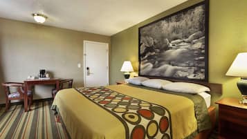 A hotel room with a bed, a desk, two chairs, a lamp, and a painting on the wall.