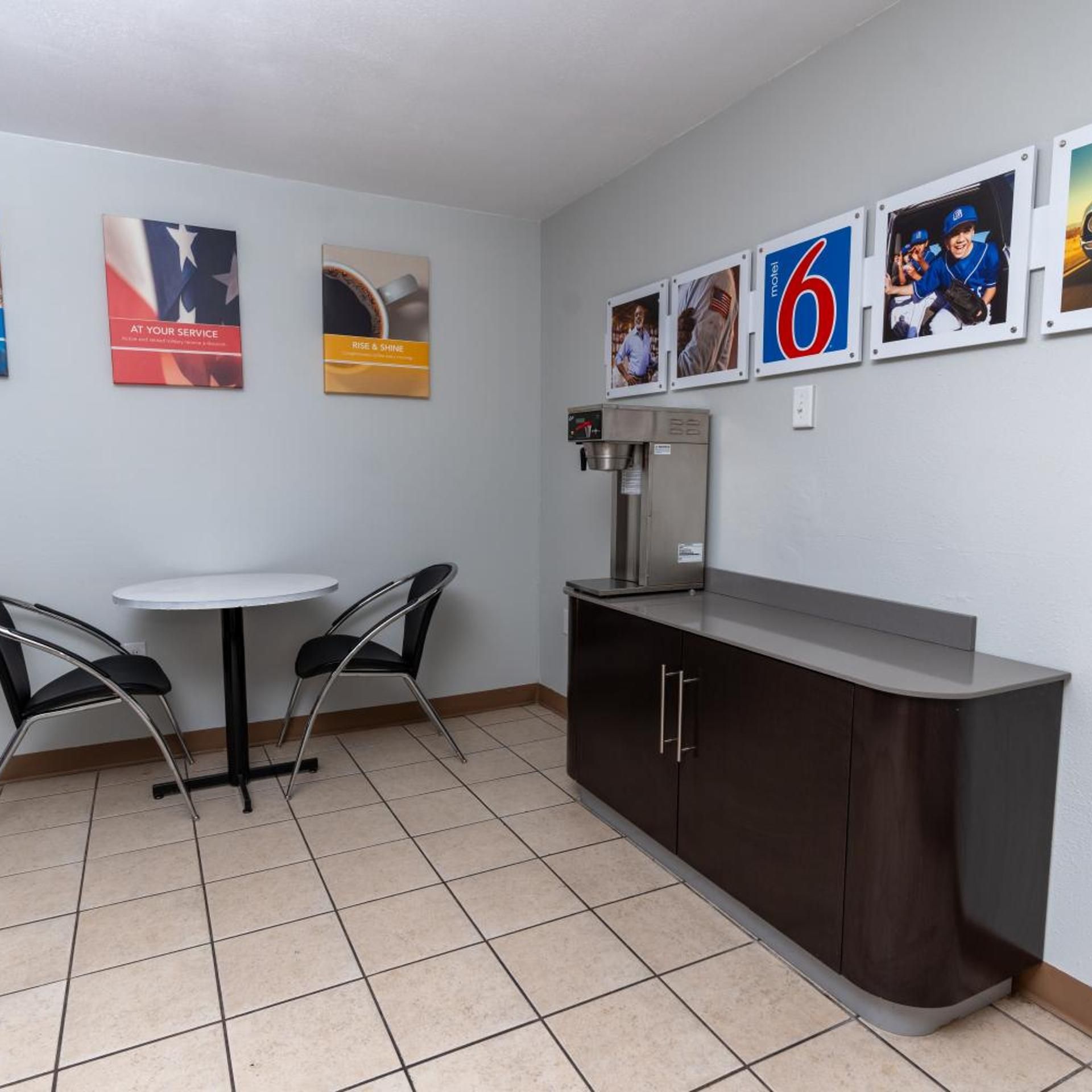 A small, clean room with a white table and two chairs, a dark cabinet, and a coffee machine.