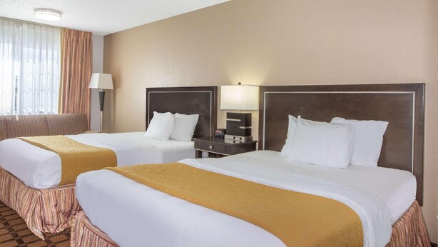 A hotel room with two beds, a nightstand, a lamp, and a window with curtains. - Hotel Roseburg (Roseburg)