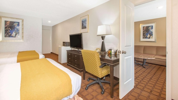 Habitación de hotel con dos camas, un escritorio con silla, televisión, lámpara y un sofá.