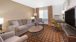 Habitación de hotel con sofá, sillones, mesa de centro, televisión y aire acondicionado.