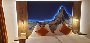 A bed with white linens and orange pillows, a wooden headboard, and a night light. - Typically Swiss Hotel Tascherhof (Taesch)