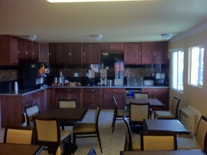 A kitchen with wooden cabinets, a microwave, and a refrigerator. There are dining tables and chairs. - First Interstate Inn (Grand Junction)