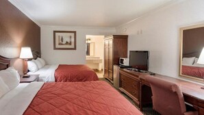 A hotel room with two beds, a desk, a television, and a mirror. - First Interstate Inn (Grand Junction)