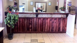 A reception desk with a wooden finish, a potted plant, and a tiled floor. - First Interstate Inn (Grand Junction)