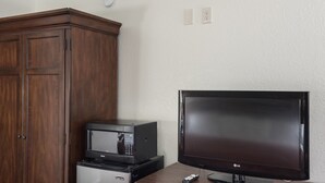 A room with a wooden cabinet, a microwave, a television, and a remote control. - First Interstate Inn (Grand Junction)