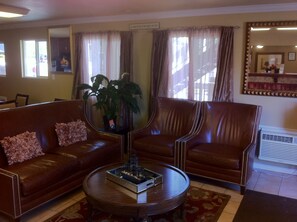 A hotel lobby with leather sofas, a round coffee table, and a large mirror. - First Interstate Inn (Grand Junction)