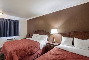 A hotel room with two beds, a nightstand with a lamp, a window with curtains, and an air conditioning unit. - First Interstate Inn (Grand Junction)