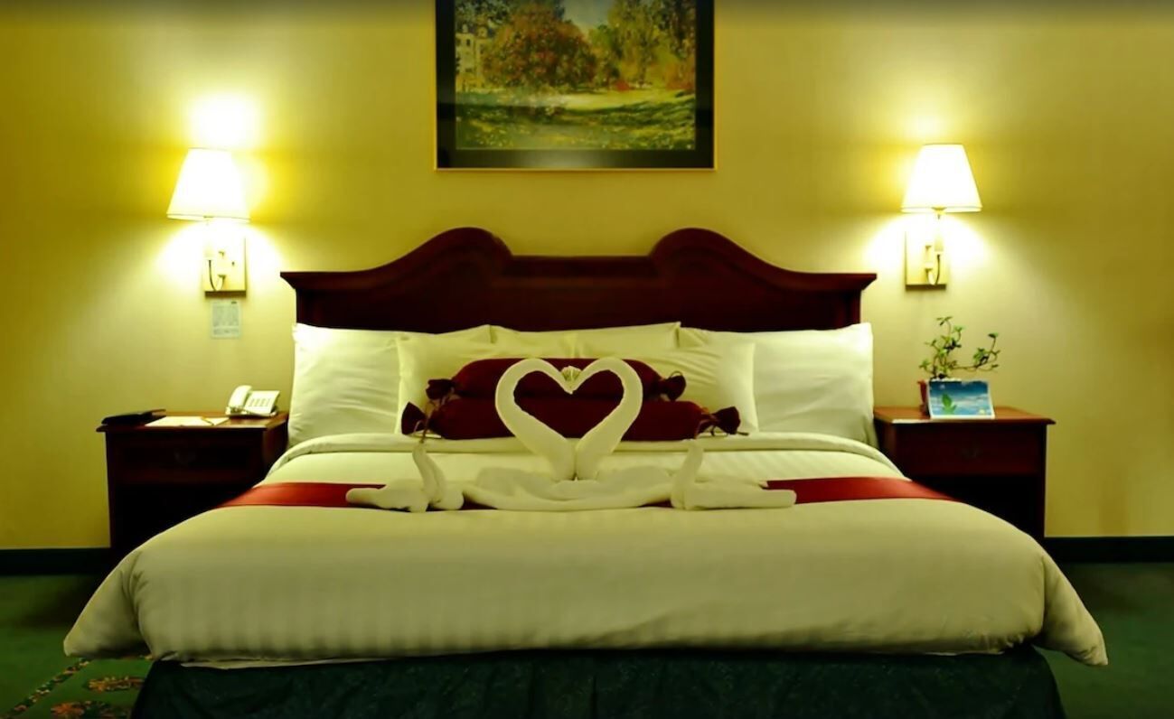 A hotel room with a large bed, two bedside lamps, a painting on the wall, and a small table with a plant.