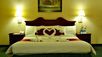 A hotel room with a large bed, two bedside lamps, a painting on the wall, and a small table with a plant.