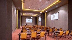 A conference room with rows of tables and chairs, a podium, and presentation screens.