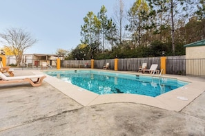 Ein rechteckiger Swimmingpool mit einer Holzterrasse, umgeben von einem Holzzaun, ausgestattet mit Liegestühlen.