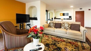 Un hall de hotel con un sofá, sillón, televisión y una recepción.