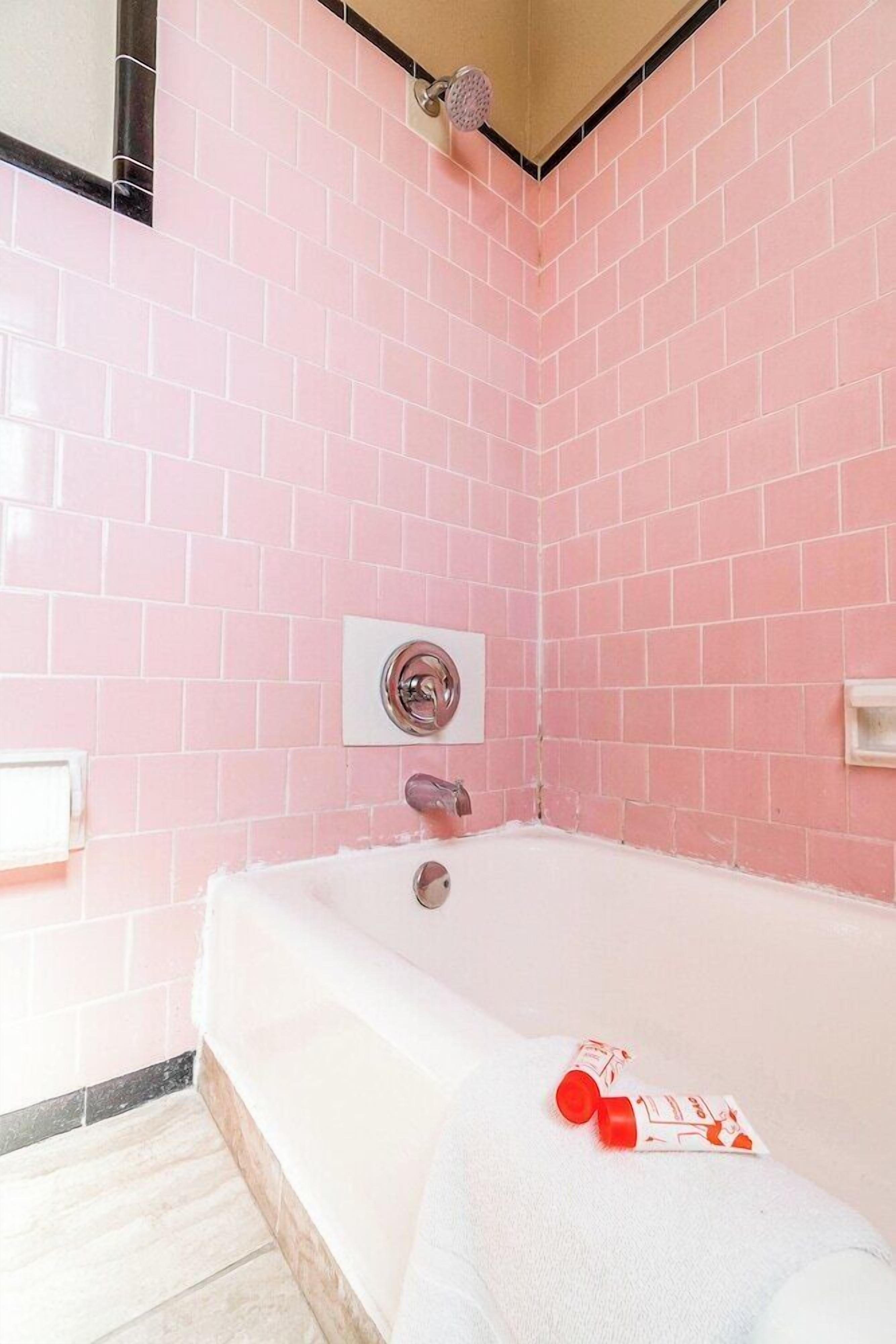 A bathroom with pink tiled walls, a white bathtub, and a showerhead.