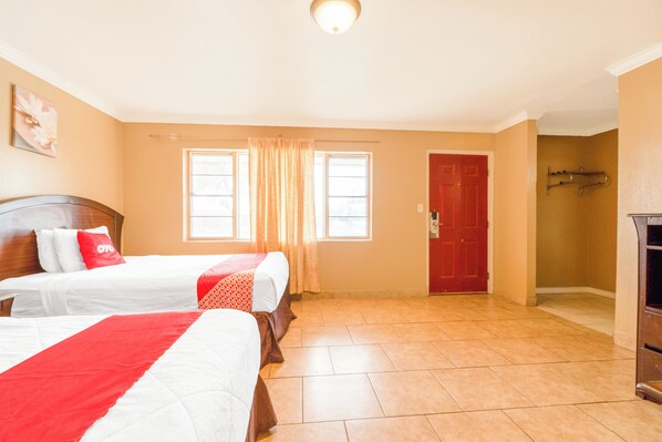 Una habitación de hotel con dos camas, una puerta roja y un ventanal grande con cortinas.