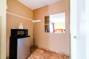 A compact kitchen with a microwave and refrigerator, a small window, and a door leading to another room. - OYO Hotel Beeville US 181 (Beeville)