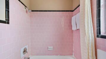 A bathroom with pink tiles, a white bathtub, a shower curtain, and a towel rack.