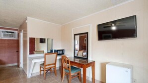 Una habitación compacta con un televisor montado en la pared, una mesita con dos sillas, un microondas y un refrigerador.