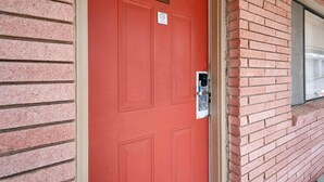 Una puerta roja con una placa de número, un teclado de cierre y una ventana a la derecha.