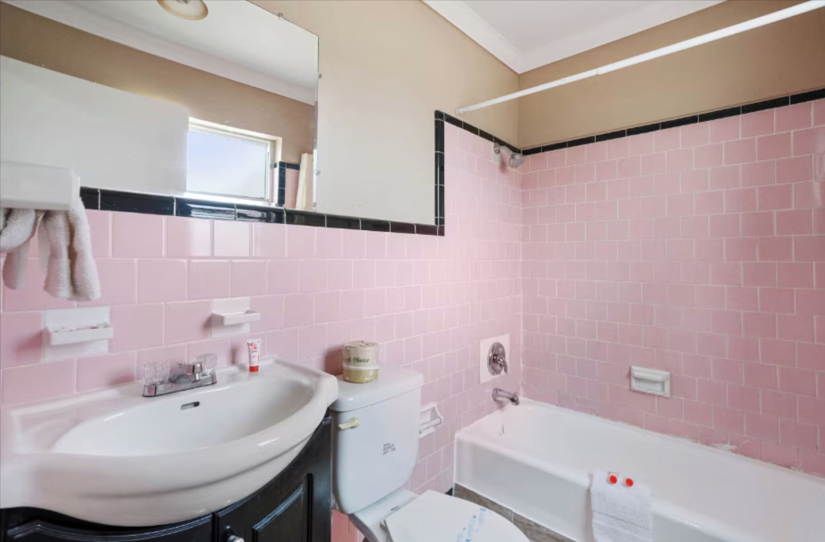 Une salle de bain avec des carreaux roses, un lavabo blanc, des toilettes et une baignoire.