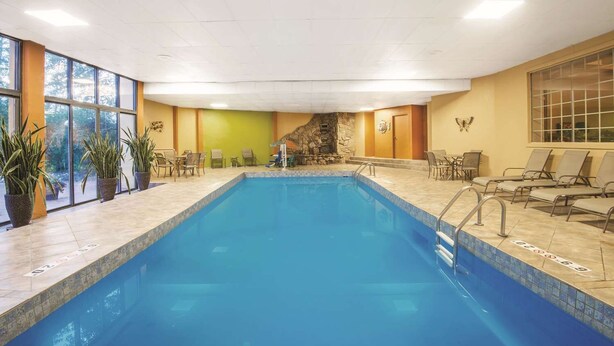 Une piscine intérieure dotée de chaises longues, de plantes en pot et d’un mur en pierre.
