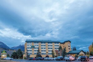 A multi-story hotel with a flat roof, a parking lot with several cars, and mountains in the background. - La Quinta Inn & Suites by Wyndham Silverthorne - Summit Co (Silverthorne)