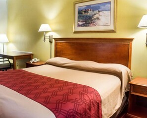 Ein Hotelzimmer mit einem hölzernen Kopfteil, einem Bett mit rotem, gemustertem Bettbezug, zwei Nachttischen mit Lampen, einem Gemälde an der Wand und einem Telefon auf dem Nachttisch.