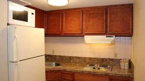 A kitchen with wooden cabinets, a white refrigerator, a microwave, a sink, and a stove. - Econo Lodge Chesapeake Route 13 and I-464 (Chesapeake)