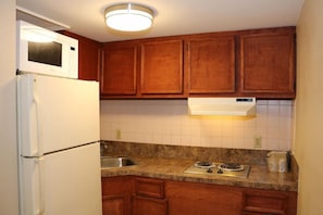 A kitchen with wooden cabinets, a white refrigerator, a microwave, a sink, and a stove. - Econo Lodge Chesapeake Route 13 and I-464 (Chesapeake)