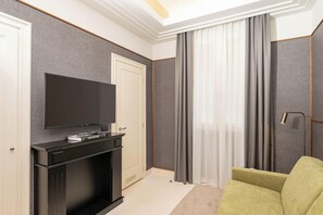 A hotel room with a flat-screen TV on a black stand, a green sofa, and a large window with curtains. - Art Hotel Novecento (Bologna)