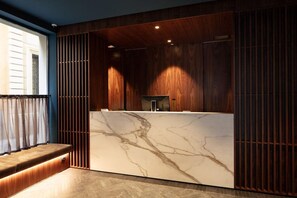 A reception desk with a marble top, wooden paneling on the walls, and a bench to the left. - Art Hotel Novecento (Bologna)