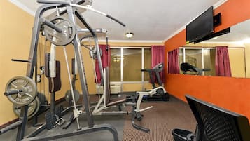 Une salle de sport équipée de matériel d’exercice, d’un tapis de course et d’un mur recouvert de miroirs.
