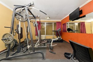 Un gimnasio con equipamiento de ejercicio, cinta de correr y un espejo grande.