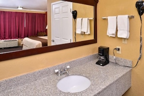 A hotel bathroom with a sink, mirror, hairdryer, and towels. - Americas Best Value Inn Schulenburg (Schulenburg)