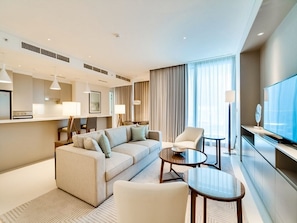 Ein modernes Hotelzimmer mit einer Sofaecke, einem Esstisch, einem Fernseher und einem großen Fenster mit Vorhängen.