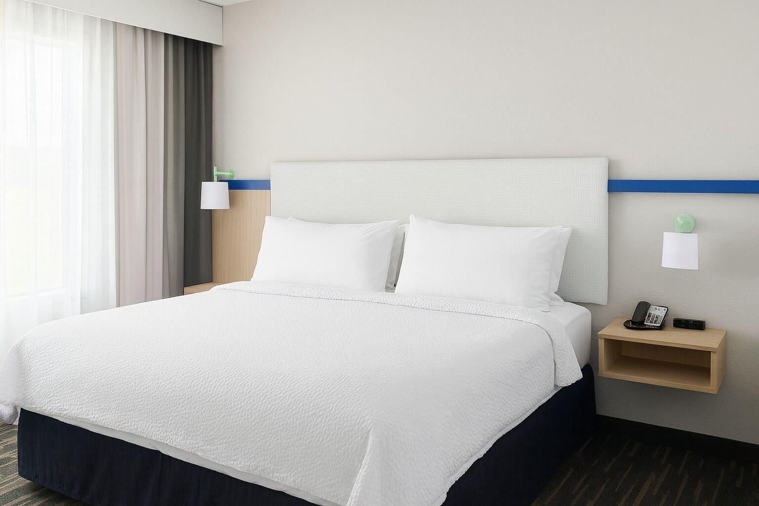 A hotel room with a bed, a nightstand, a lamp, and a wall-mounted phone.