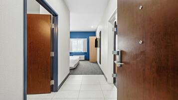 A hotel corridor with a bed, a window with curtains, and a door.