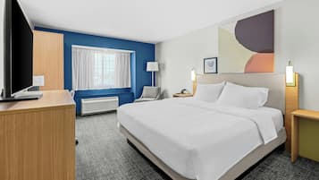 A hotel room with a large bed, a desk, a television, a window with curtains, a wall-mounted lamp, and a painting.