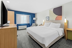 Habitación de hotel con una cama grande, un escritorio, televisor, ventana con cortinas, lámpara de pared y un cuadro.