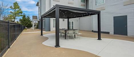 Un patio techado con una mesa y sillas, junto a un edificio de fachada gris.